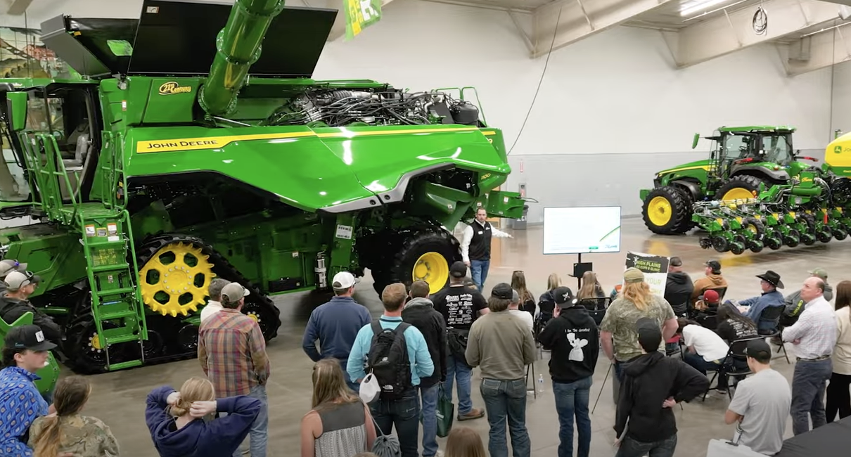 A group of people watching a demonstration on a piece of John Deere equipment.